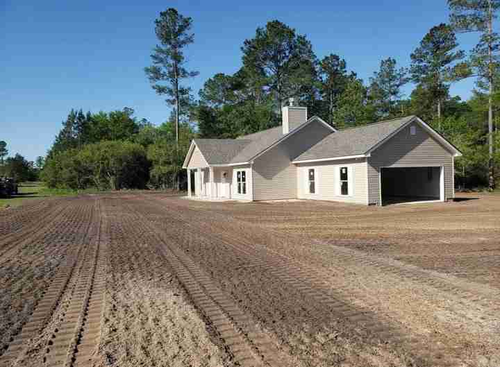 Rural house with plowed field and trees.